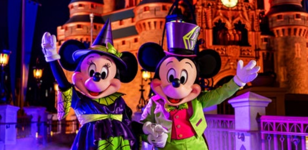 Mickey and Minnie Mouse in Halloween costumes posing in front of Cinderella Castle lit in spooky purple and orange at Magic Kingdom Park.