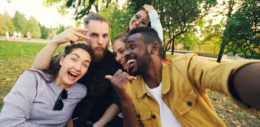 Group of diverse friends smiling and taking a selfie outdoors in a park during fall.