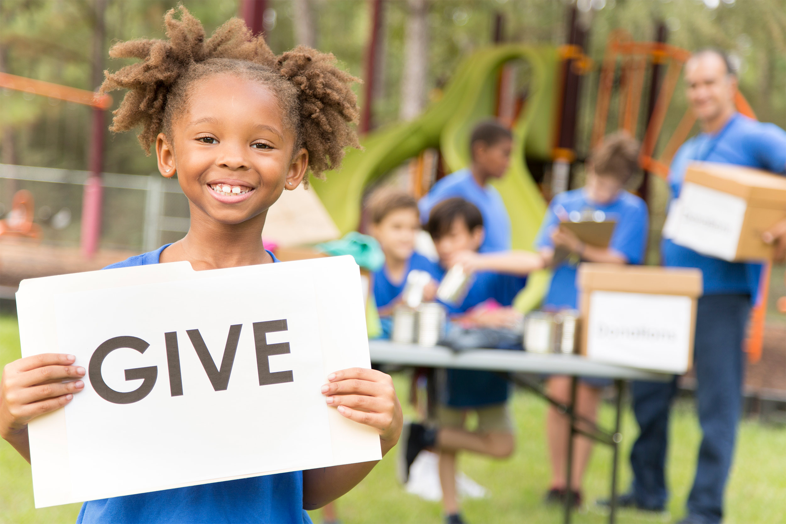 Young girl holding a sign that reads 'Give' during a volunteer event