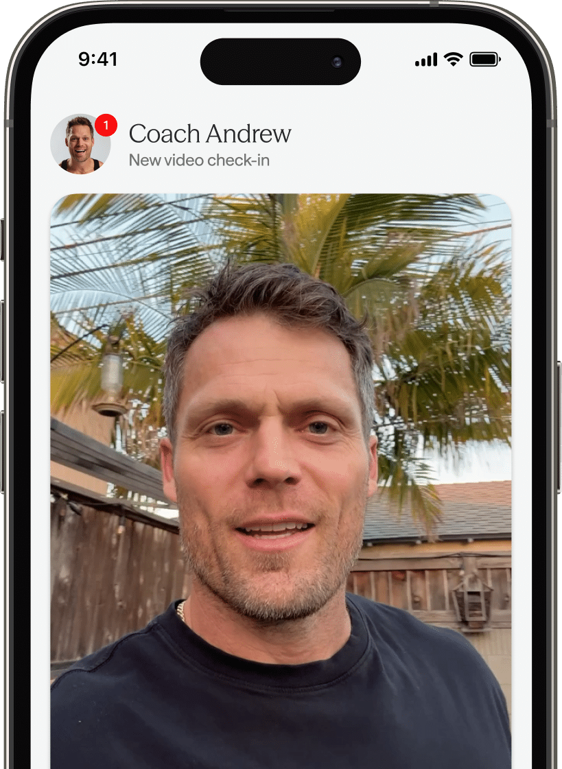 A smartphone screen displays a video check-in notification from 'Coach Andrew', a man with short brown hair outdoors with palm trees in the background. A nearby chat bubble reads, 'Nice lift, Alex! You recovered quickly between sets. That Zone 2 work is paying off 💪.'