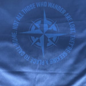 A compass rose encircled by the words 'Not all those who wander are lost, they're seeking a place to call home'