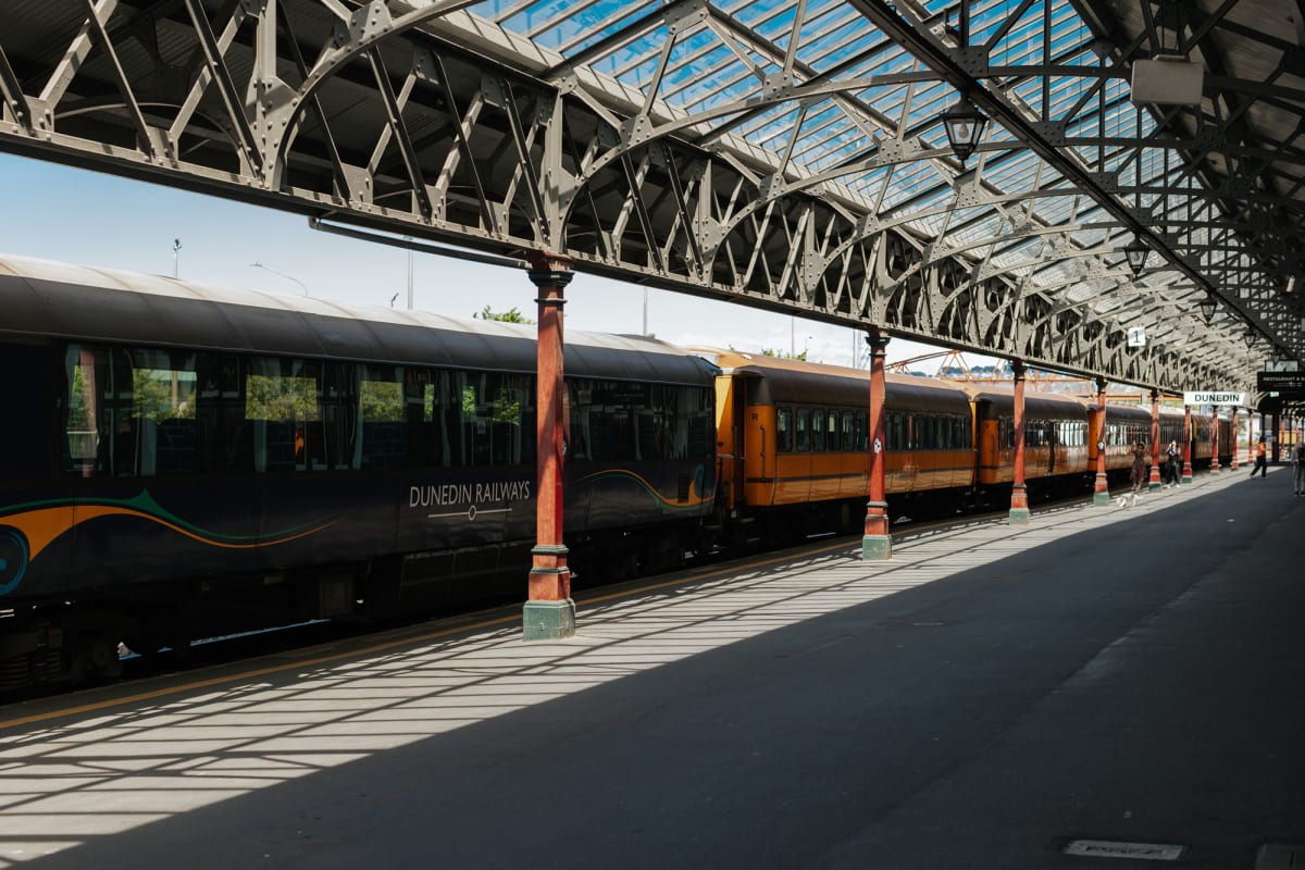 The Taieri gorge passenger train parked at the Dunedin Railway Station beneath a large glass and steel roof.