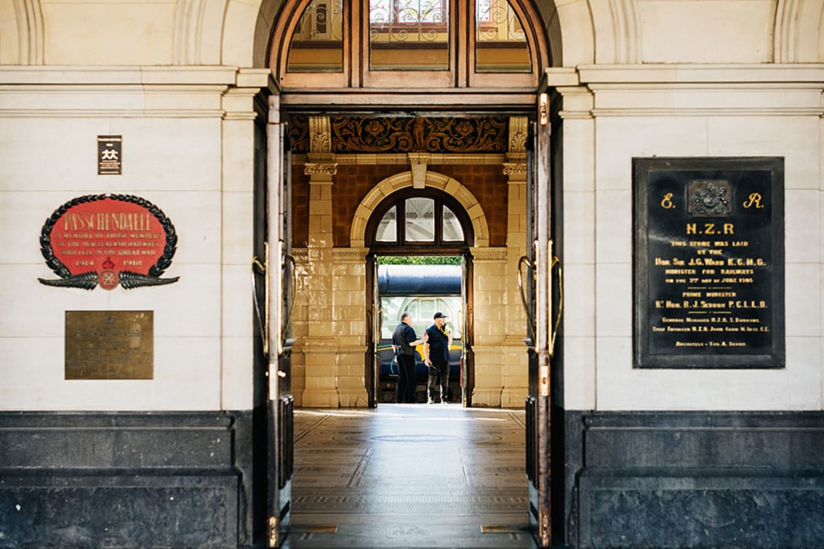 Two Dunedin railway station staff stand talking in an open doorway of the historic Dunedin brick station building.