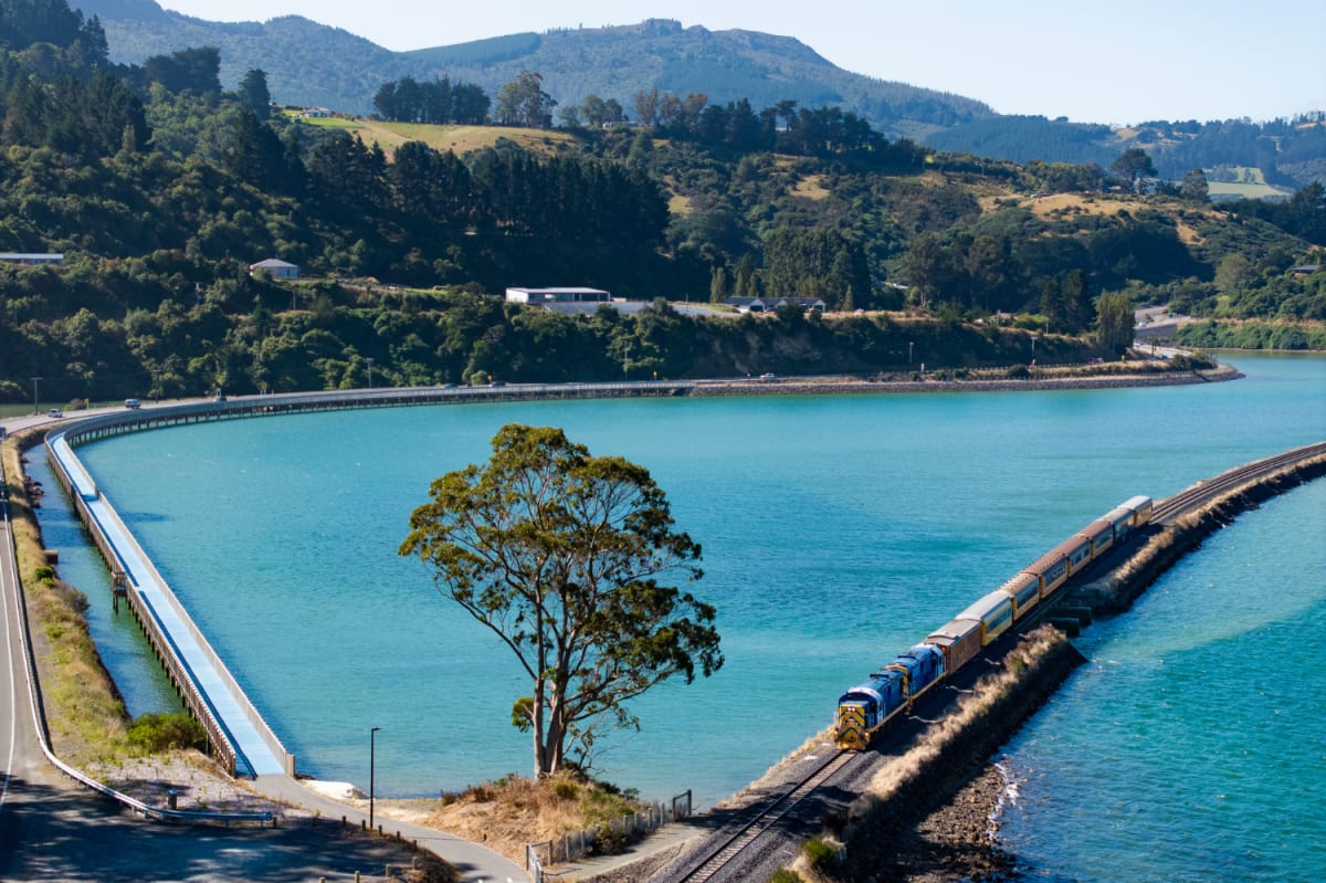 The Seasider train travels along a coastal railway track beside a turquoise bay.