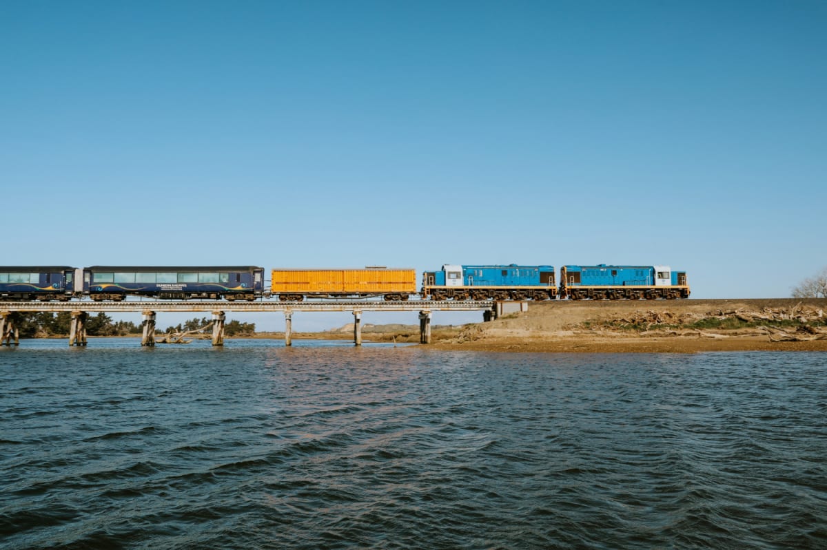 The Seasider Train crosses a concrete bridge over a body of water under a clear blue sky.