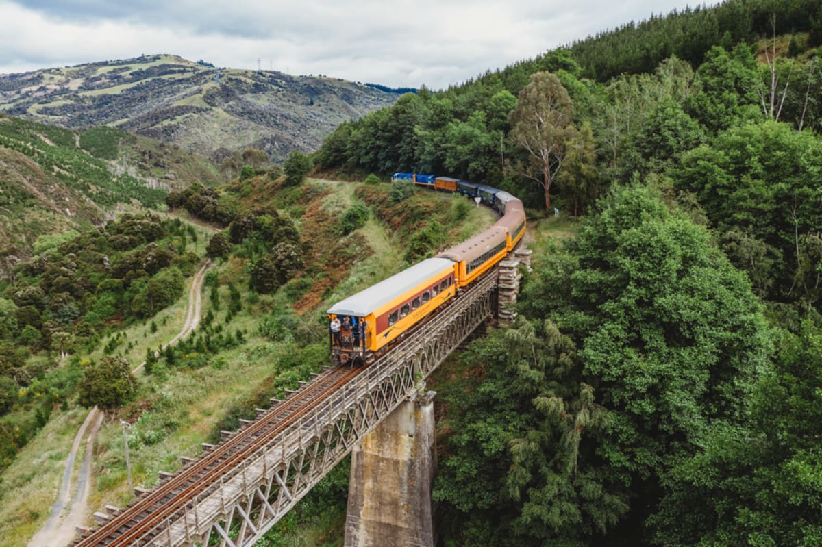 The Taieri Gorge train crosses one of the stone viaducts through the lush, Otago hilly valley with the winding Taieri river below.