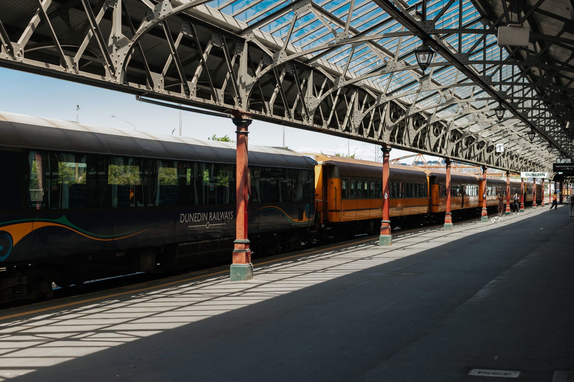 The Taieri gorge passenger train parked at the Dunedin Railway Station beneath a large glass and steel roof.