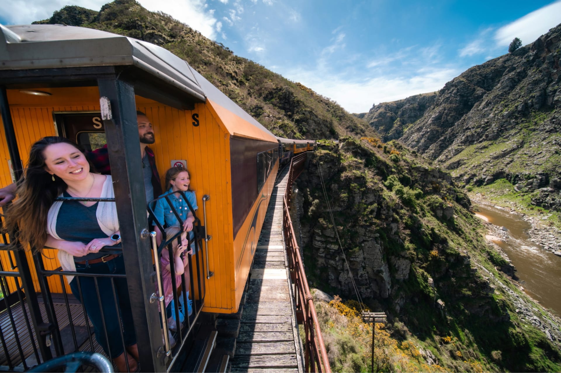 Passengers on the Taieri Gorge train look out over the winding Taieri river gorge in a mountainous Otago landscape.