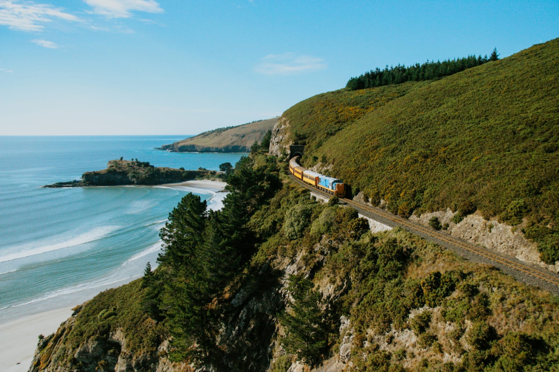 The Seasider train with panoramic windows crosses a bridge over a calm body of water.