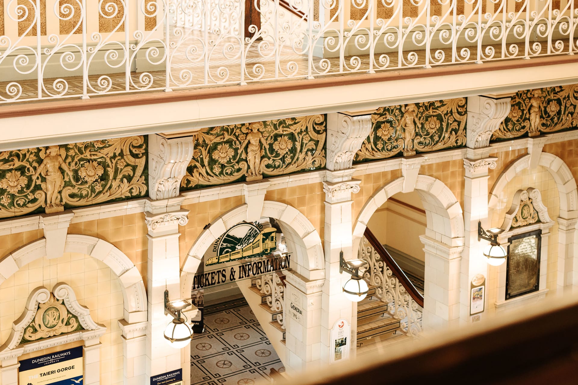 An aerial view of the historic Dunedin Railway Station in New Zealand, featuring formal gardens and a seagull flying in the foreground.