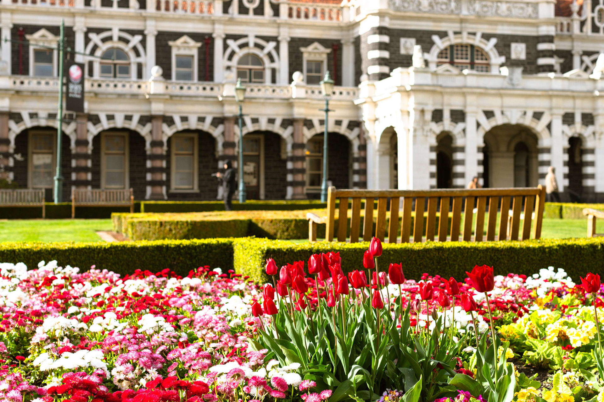 The ornate stone exterior and dark brown roof of the Dunedin Railway Station against a clear blue sky.