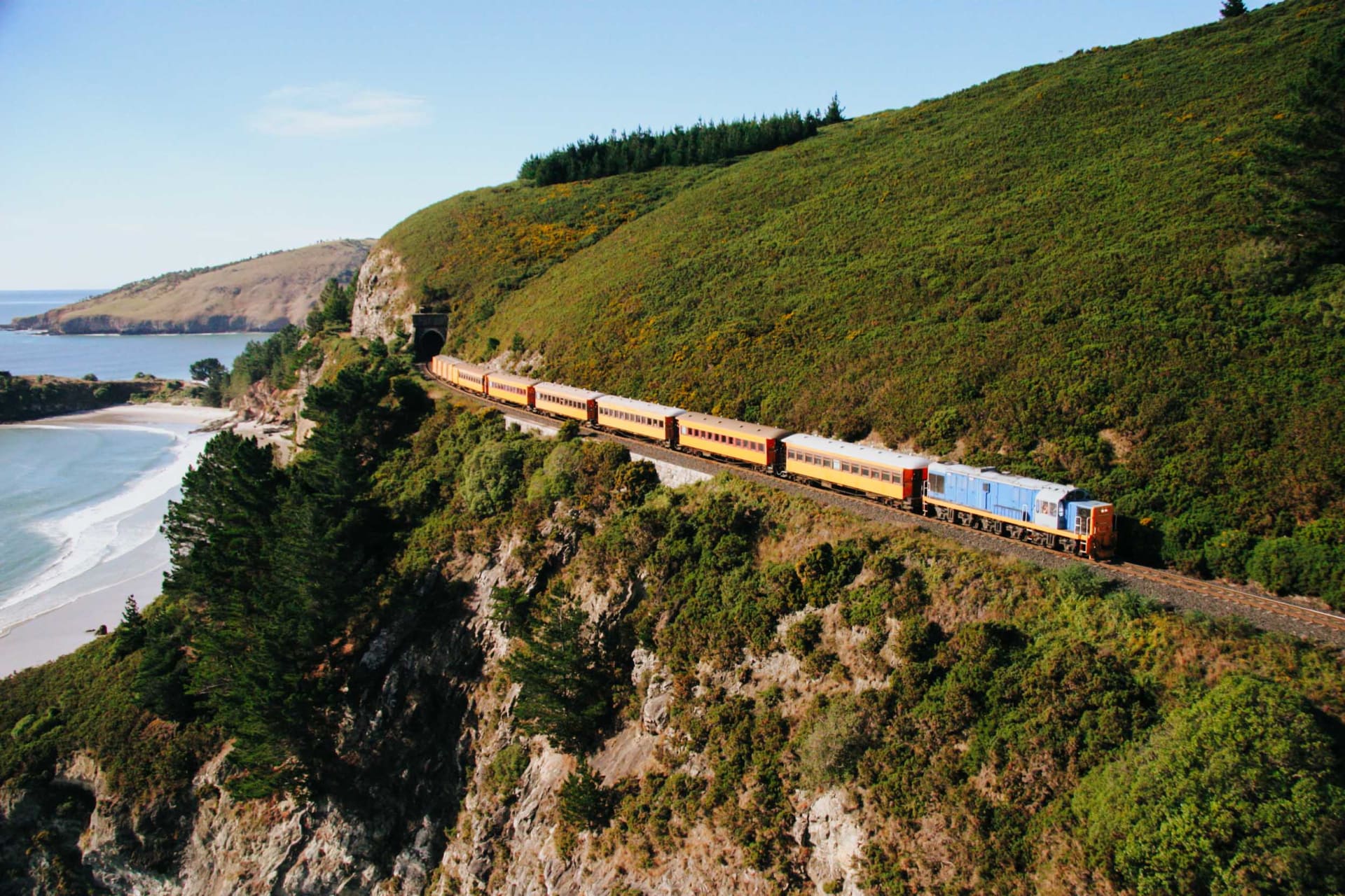 The Seasider train with panoramic windows crosses a bridge over a calm body of water.