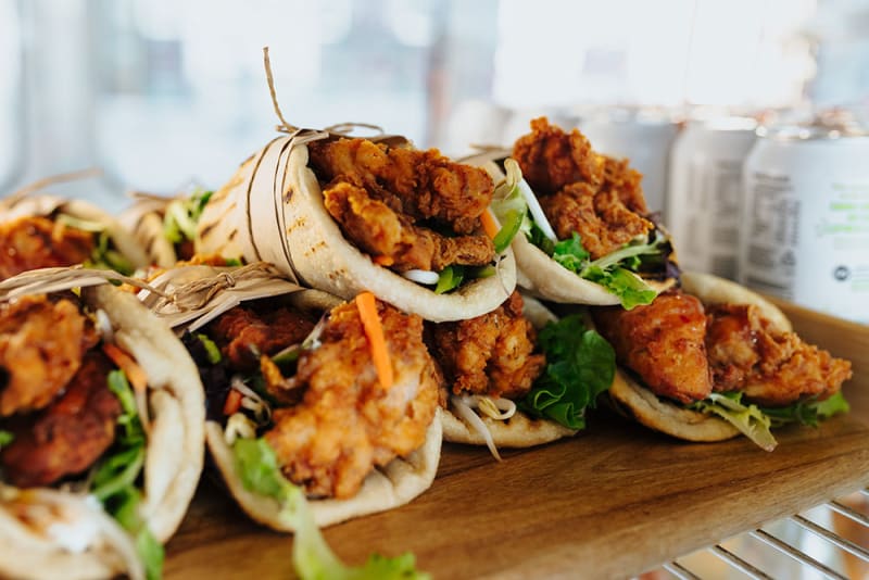 Several fried chicken wraps with lettuce and carrots on a wooden tray.