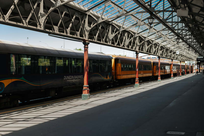 The Taieri gorge passenger train parked at the Dunedin Railway Station beneath a large glass and steel roof.