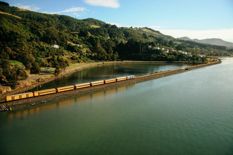 The Seasider train with panoramic windows crosses a bridge over a calm body of water.