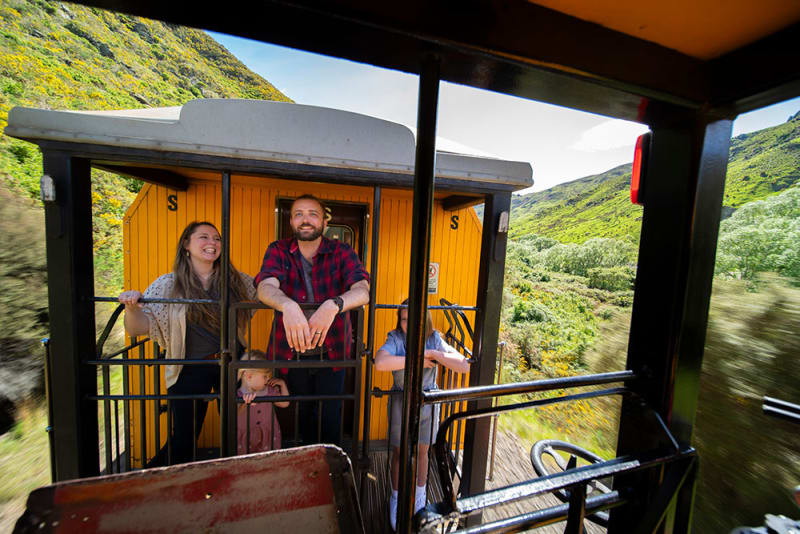 Two women inside the Taieri Gorge train car point excitedly out the window at a mountain landscape.