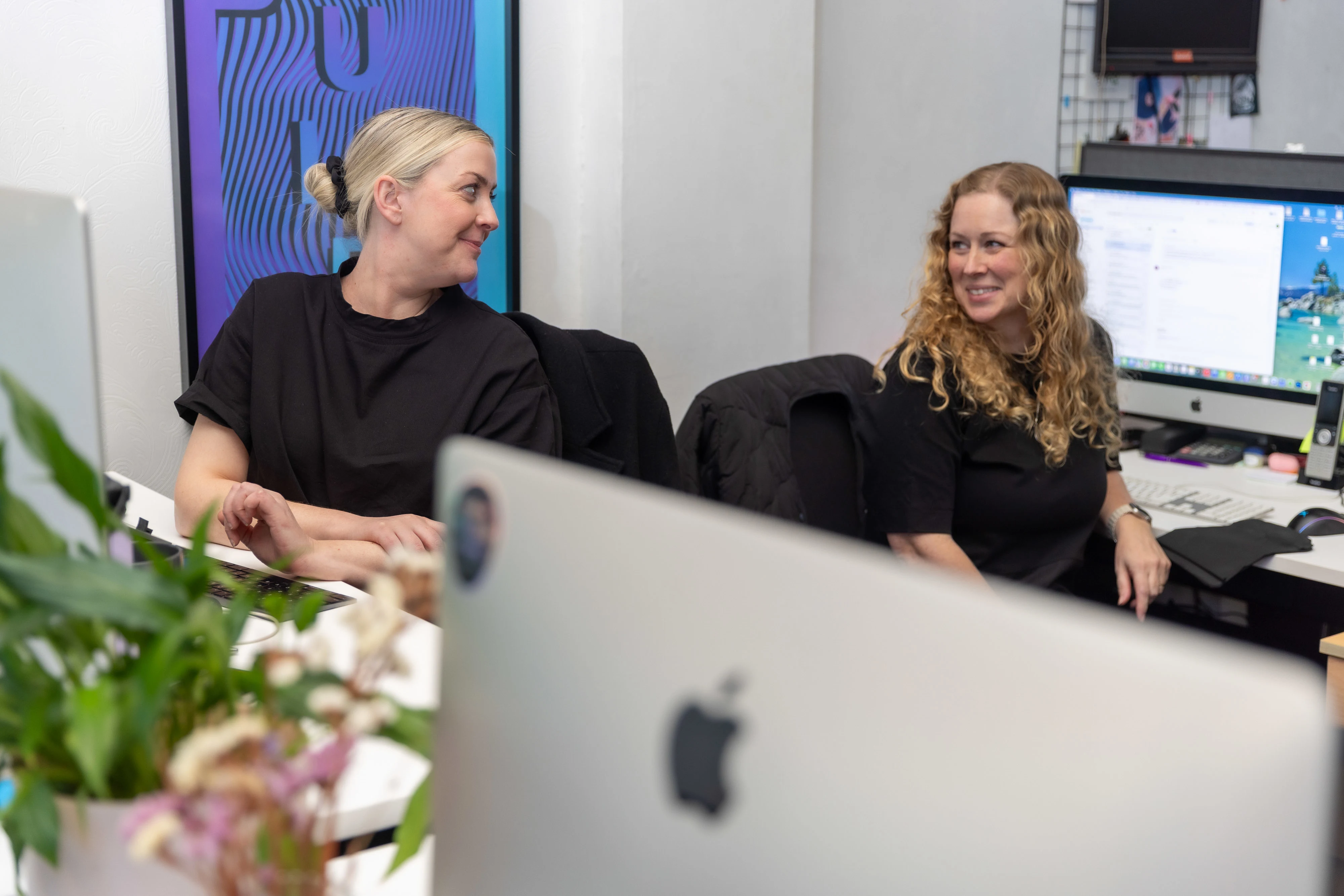 Georgina and Leigh chat at their desks in the Firebrand office.