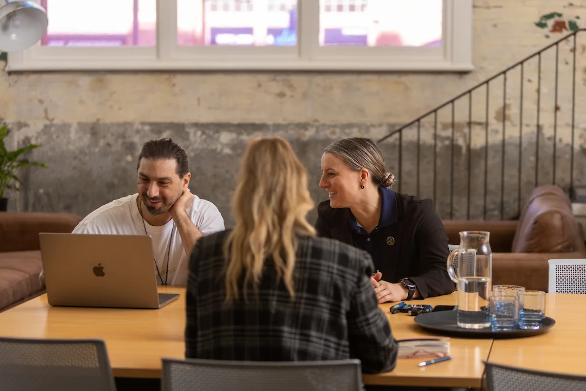 Malcolm chats with two colleagues around a table in the Firebrand office.
