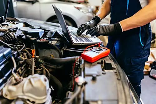 Mechanic using a diagnostic tool and laptop on a car engine