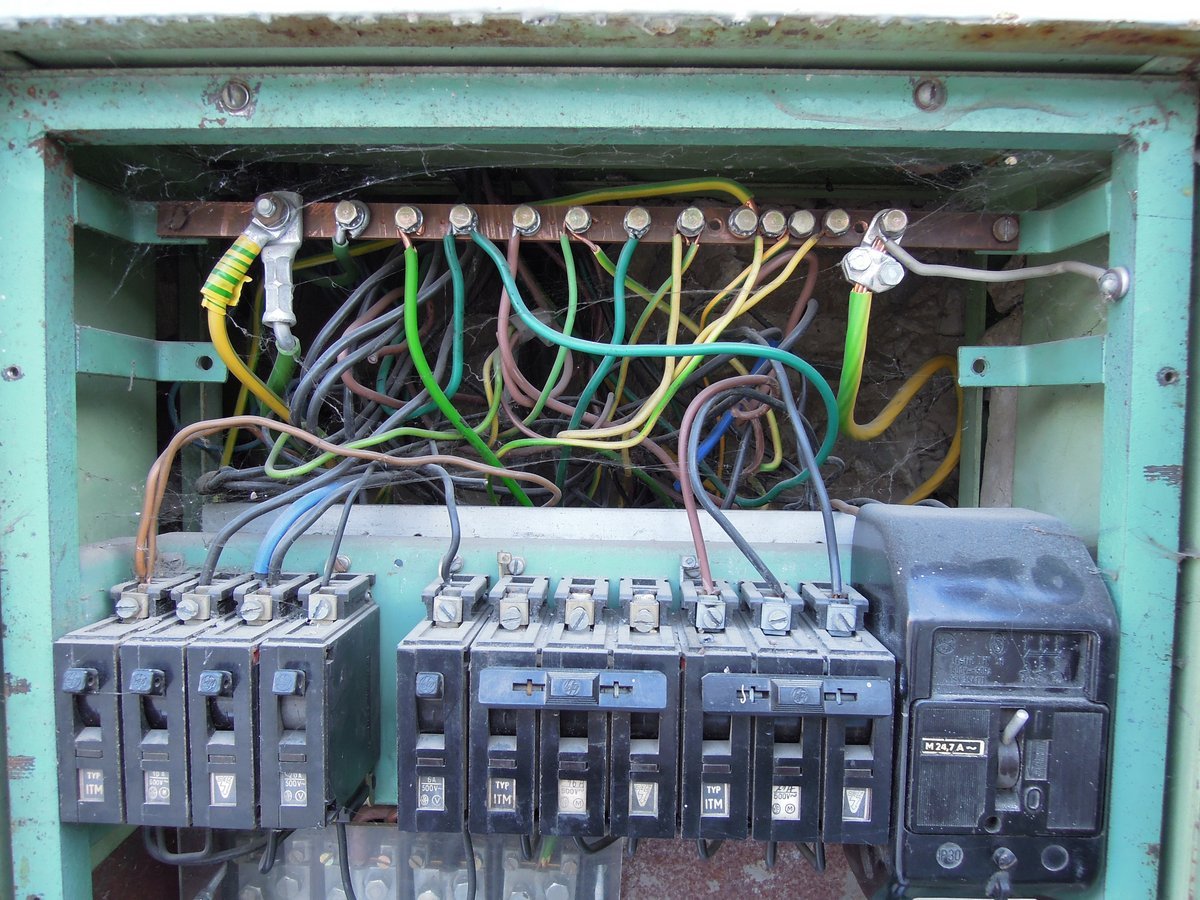 An old metal distribution board with its cover off, showing a row of breakers and a tangle of coloured wires