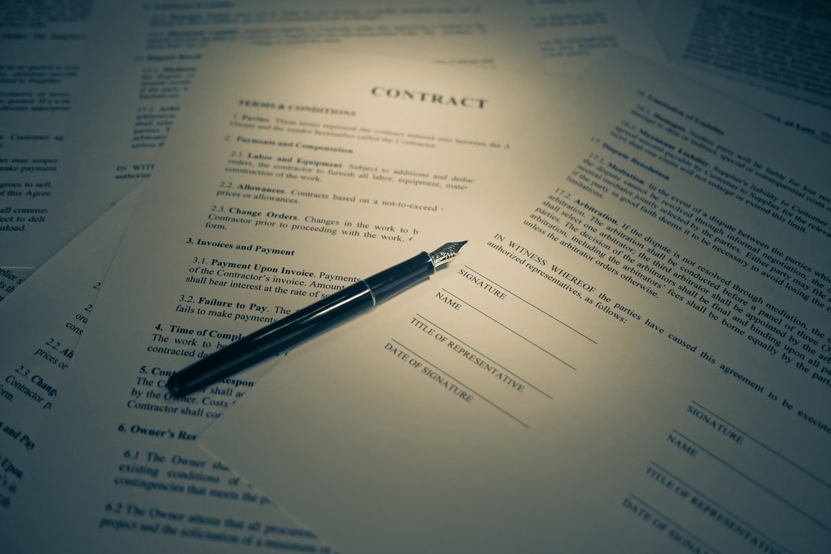A printed contract lying on a desk with a fountain pen resting across the signature section