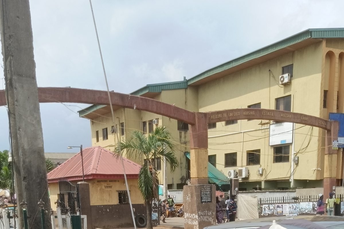 The arched main gate of Abesan Housing Estate in Ipaja, Lagos, with a gatehouse and a three-storey block behind it