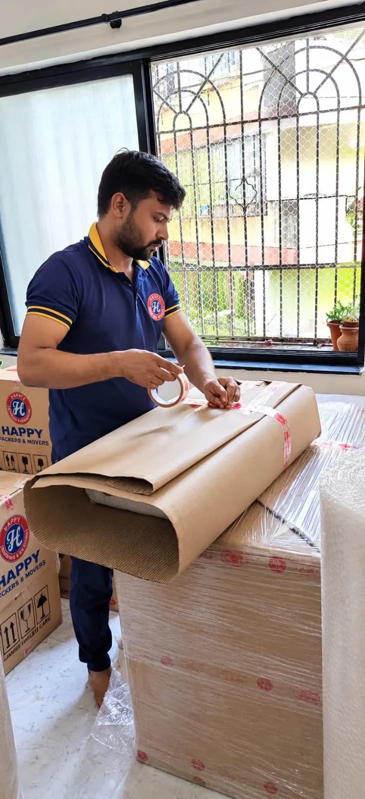 A Happy Packers and Movers packer wrapping furniture in corrugated paper and tape