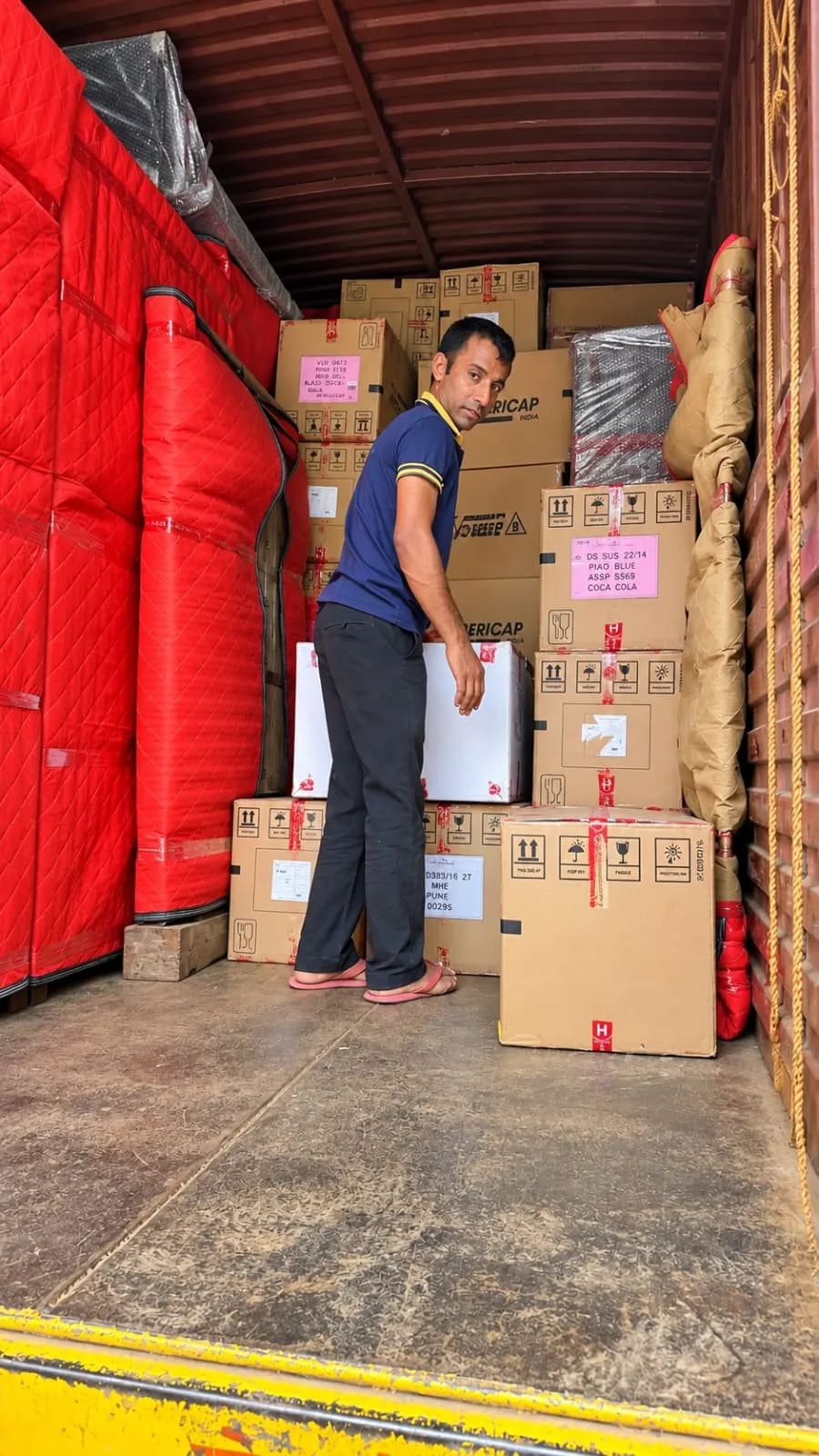 A crew member stacking cartons and padded furniture inside a moving truck