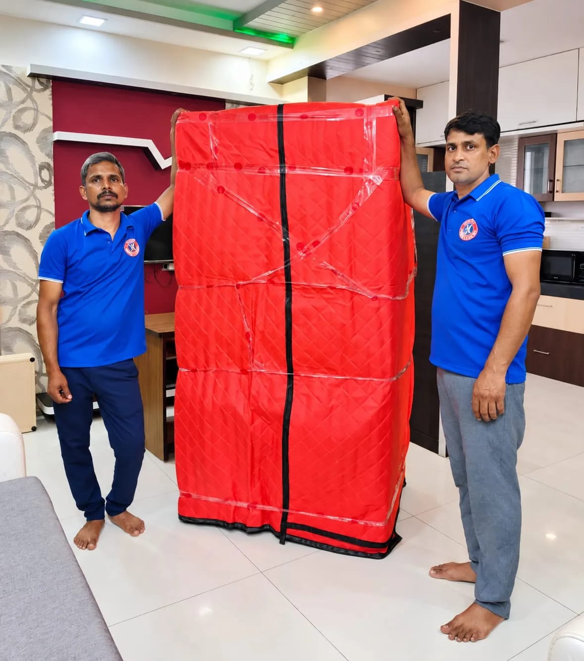 Two Happy Packers and Movers crew members with a wardrobe wrapped in a red quilted cover