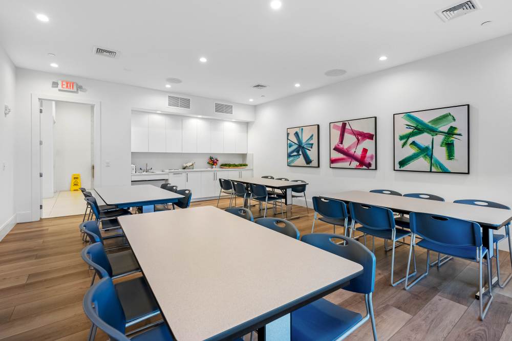 Modern community room with wood-style flooring, tables, and colorful wall art at Solera at Avalon Trails in Delray Beach, Florida