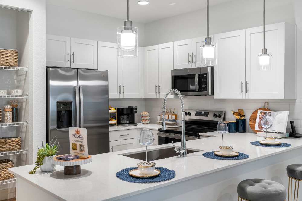 Modern kitchen with stainless steel appliances, granite countertops, and pendant lights over a spacious island at Solera at Avalon Trails in Delray Beach, Florida