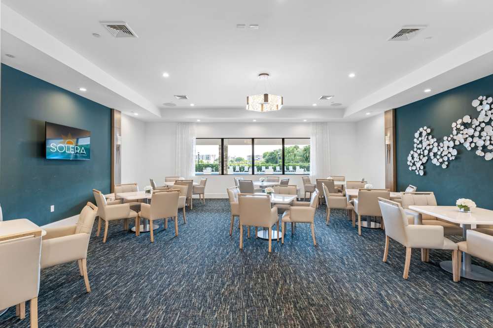 Bright dining area with modern furniture, large windows, and decorative wall art at Solera at Avalon Trails in Delray Beach, Florida