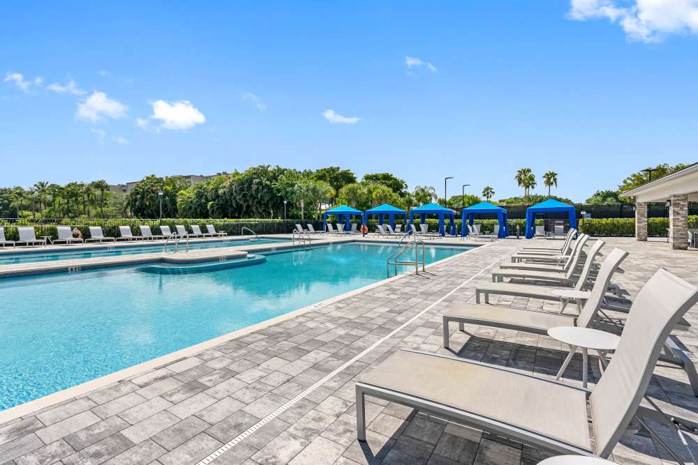 Sparkling resort-style pool with lounge chairs and shaded cabanas surrounded by lush greenery at Solera at Avalon Trails in Delray Beach, Florida