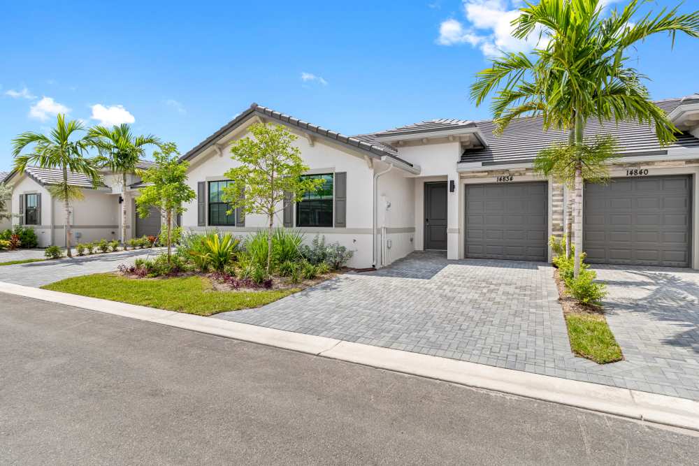 Modern apartment community with lush landscaping, paver driveway, and palm trees under a clear blue sky at Solera at Avalon Trails in Delray Beach, Florida