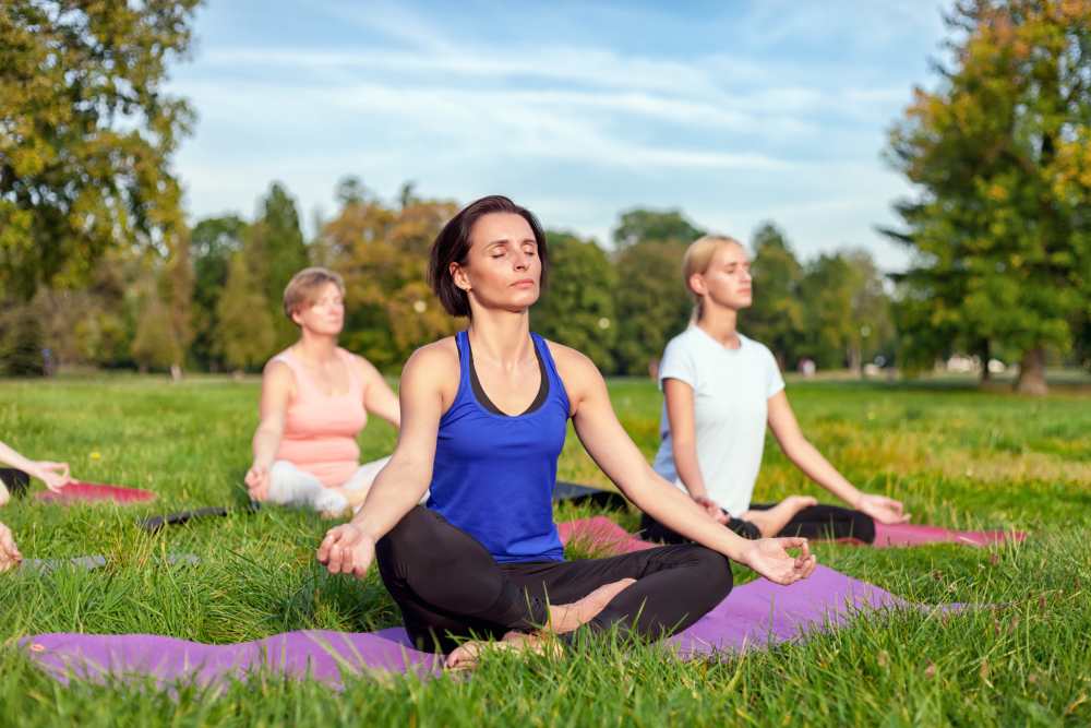 Group of women practicing yoga on mats in a green park under a clear sky at Solera at Avalon Trails in Delray Beach, Florida