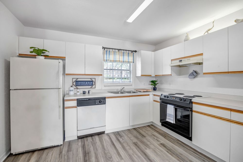 Open kitchen with white appliances, storage spaces and wood-style flooring at Carlton Arms Of North Lakeland in Lakeland, Florida
