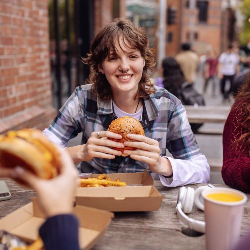 Woman enjoying burger and fries at outdoor table near Redwood in San Marcos, Texas