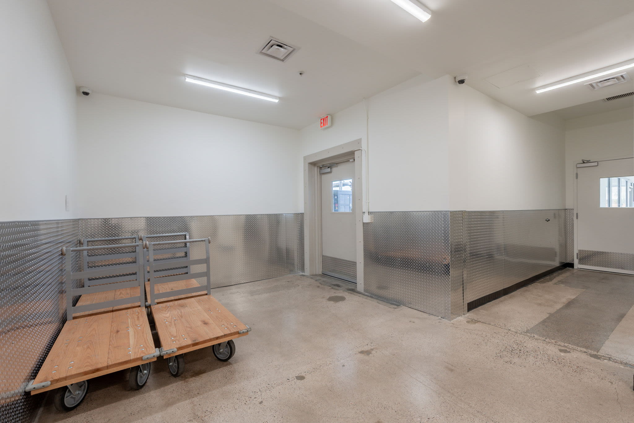 Empty hallway with carts, diamond plate walls, and an exit door at the end at Park Central Self Storage in Phoenix, Arizona