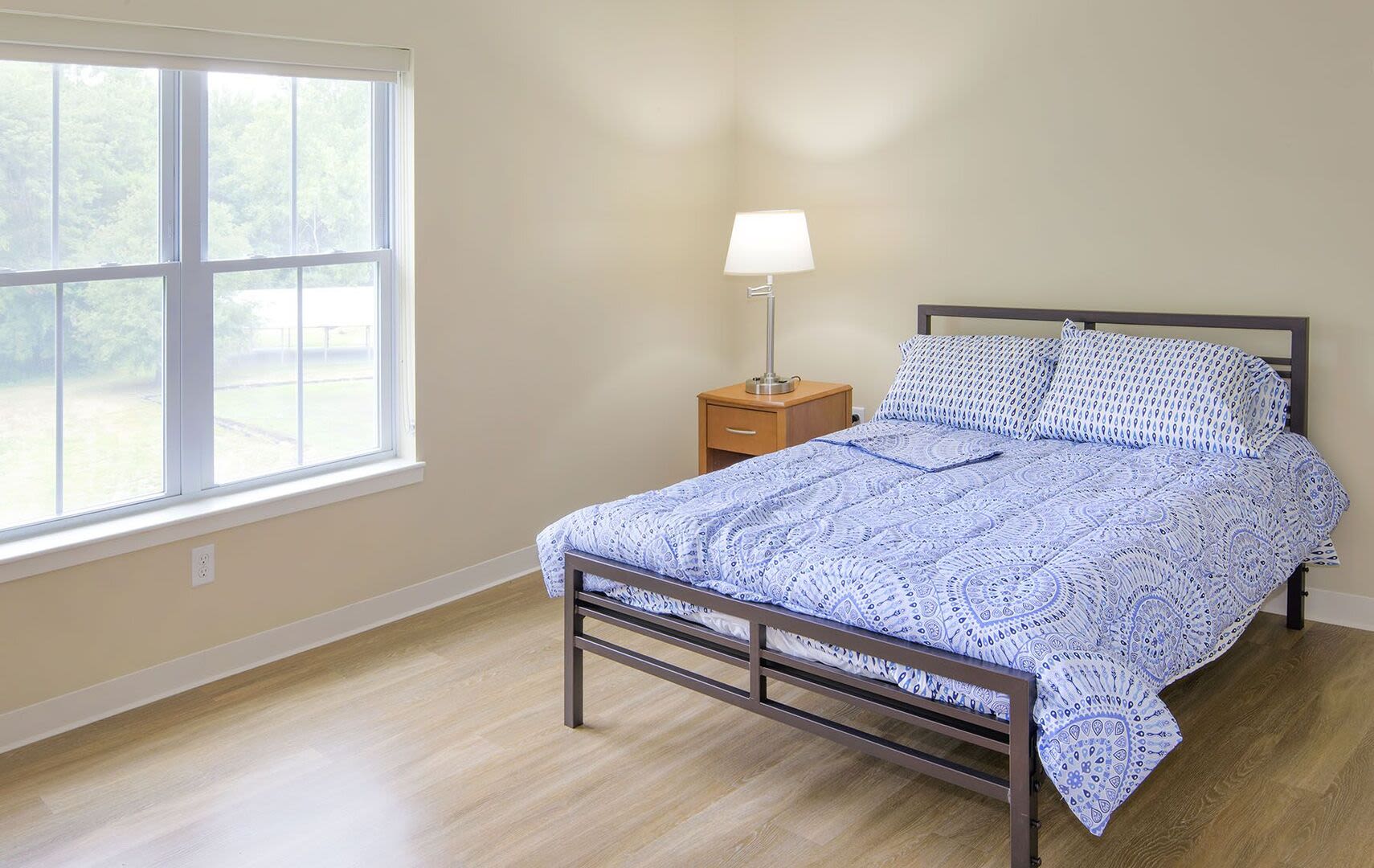 Spacious bedroom with king size bed, side table with lamp and large window at Bedford Green Apartments in Bedford, Massachusetts