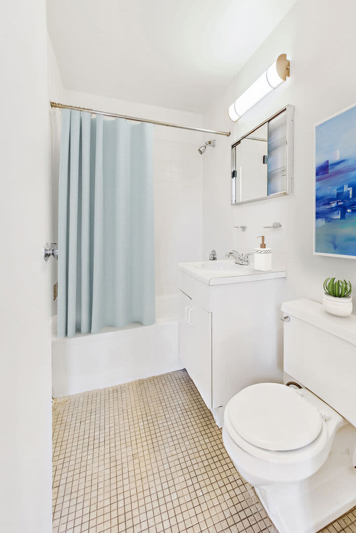 Well-lit tile flooring bathroom with standard bath tub, vanity and commode at Mercantile Wharf in Boston, Massachusetts