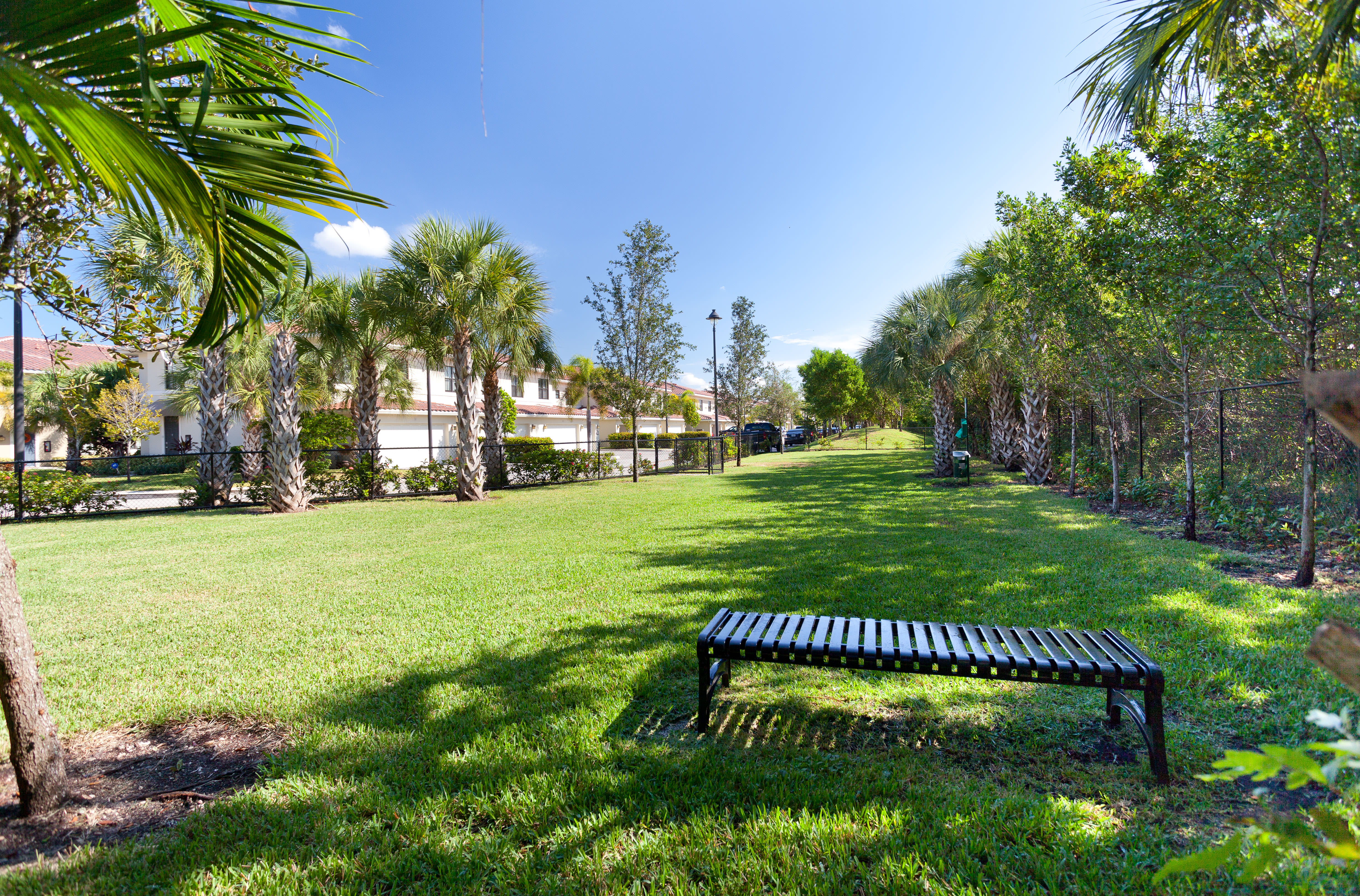 Fenced onsite dog park with lush grass and a bench at The Residences at Lakehouse in Miami Lakes, Florida