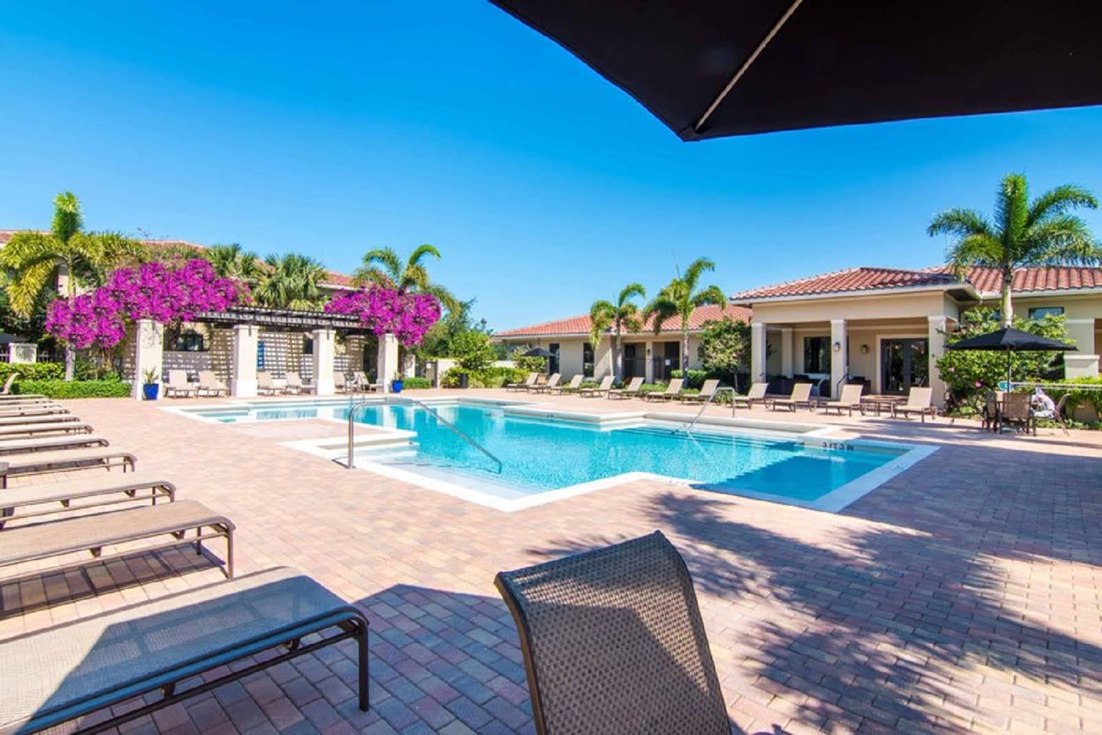 Resort-style swimming pool surrounded by lounge chairs and tables with umbrellas at The Residences at Lakehouse in Miami Lakes, Florida