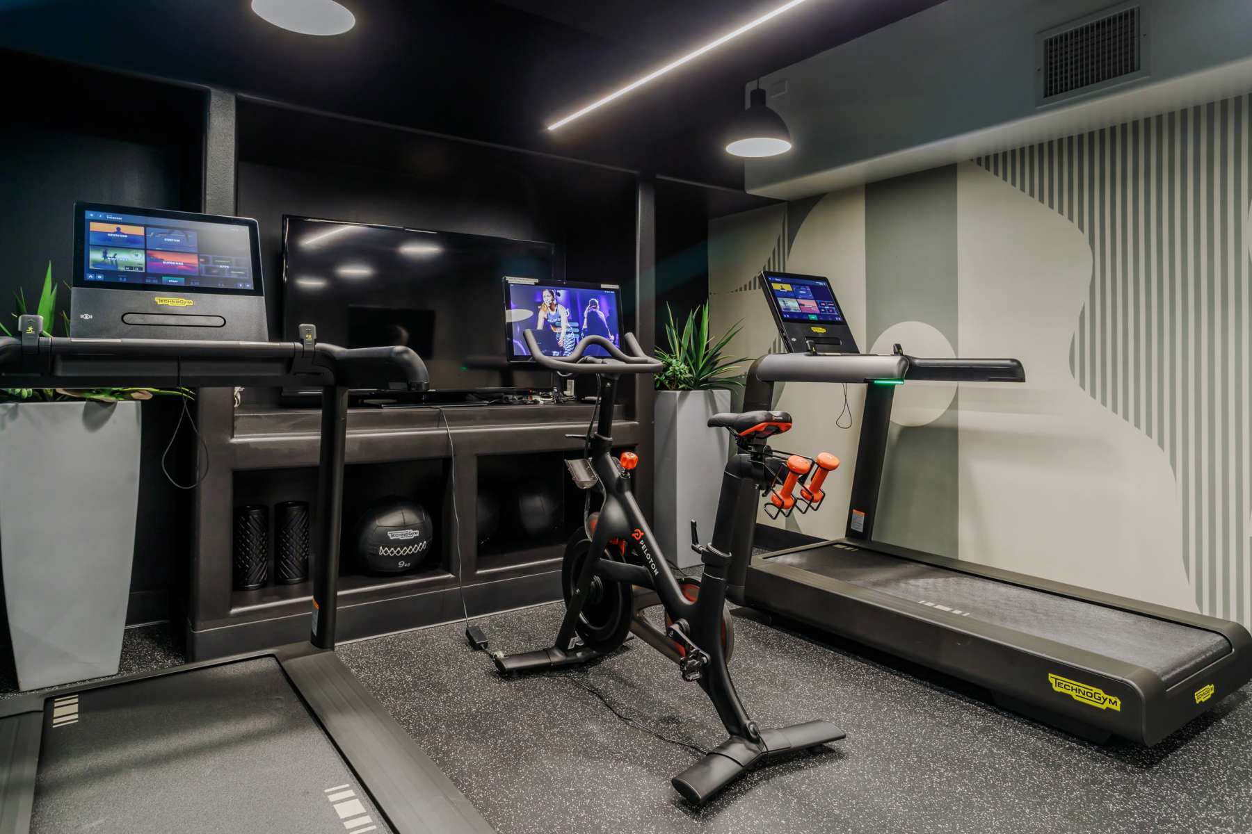 Indoor gym with treadmills, Peloton bike, wall-mounted TV, foam rollers at Luxe Villas in Brentwood, California