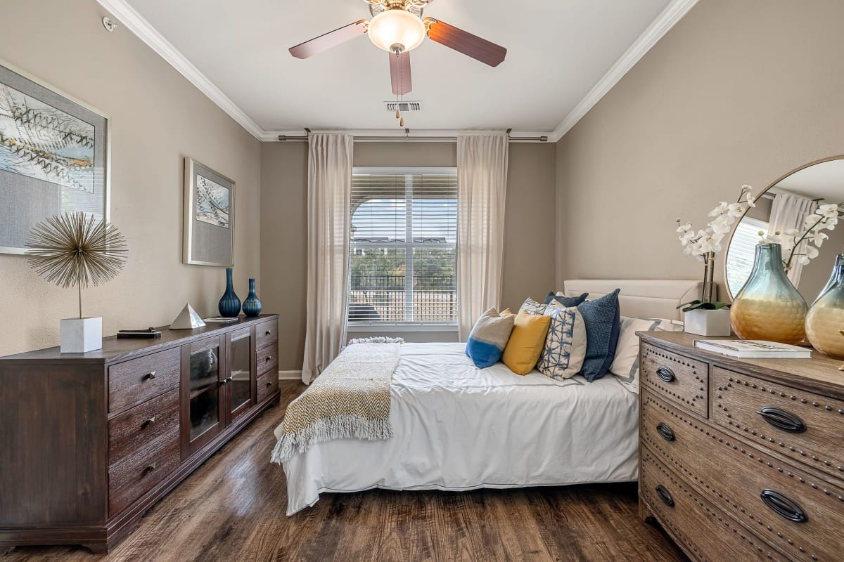 Bright and cheerful bedroom with wood flooring, a large window, and a ceiling fan at Marquis at Crown Ridge in San Antonio, Texas