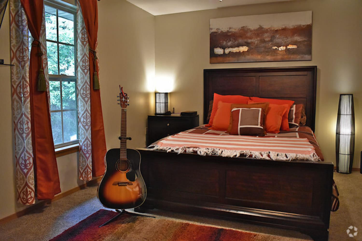 Hardwood-style flooring and draped windows in a model home's bedroom at Campbell Flats Apartments in Springfield, Missouri