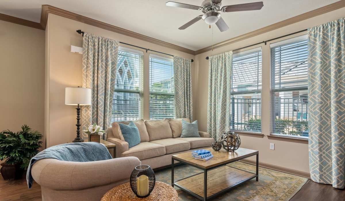 Spacious living room with large couch, chair, coffee table, ceiling fan and large windows at The Crosby at Towne Center in Sanford, Florida