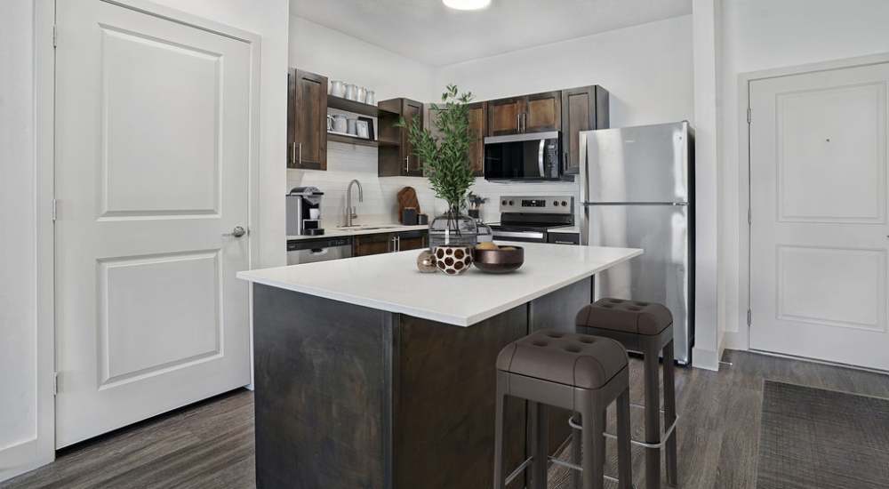 Modern kitchen with granite countertops, stainless steel appliances, and wood-style flooring, featuring an island and bar stools at Canyon View Crossing in Orem, Utah