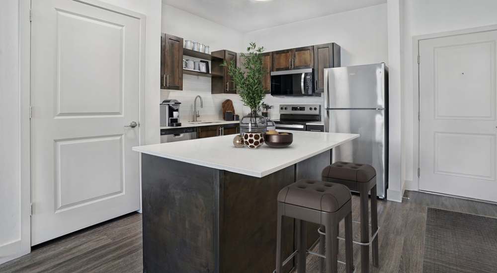 Modern kitchen with granite countertops, stainless steel appliances, and wood-style flooring, featuring an island with seating at Canyon View Crossing in Orem, Utah