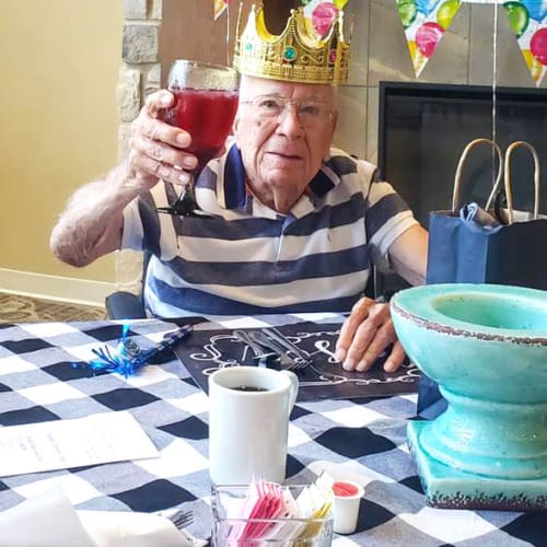 Resident wearing a crown and raising a goblet at The Oxford Grand Assisted Living & Memory Care in McKinney, Texas