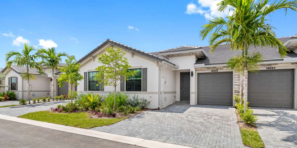 Modern apartment community with lush landscaping, paver driveway, and palm trees under a clear blue sky at Solera at Avalon Trails in Delray Beach, Florida